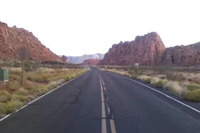 A two-lane road leading toward red and white sandstone cliffs at the entrance to Snow Canyon.