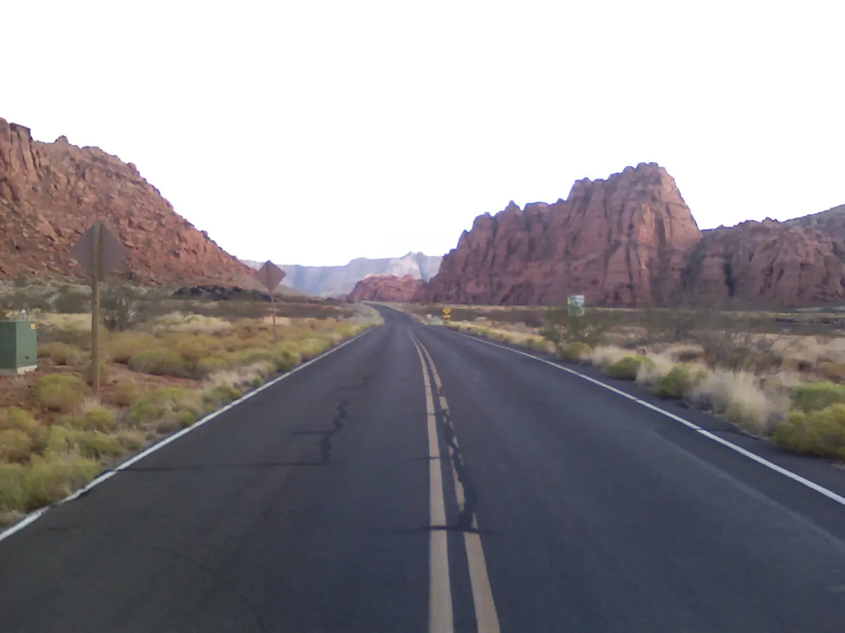 A two-lane road leading toward red and white sandstone cliffs at the entrance to Snow Canyon.
