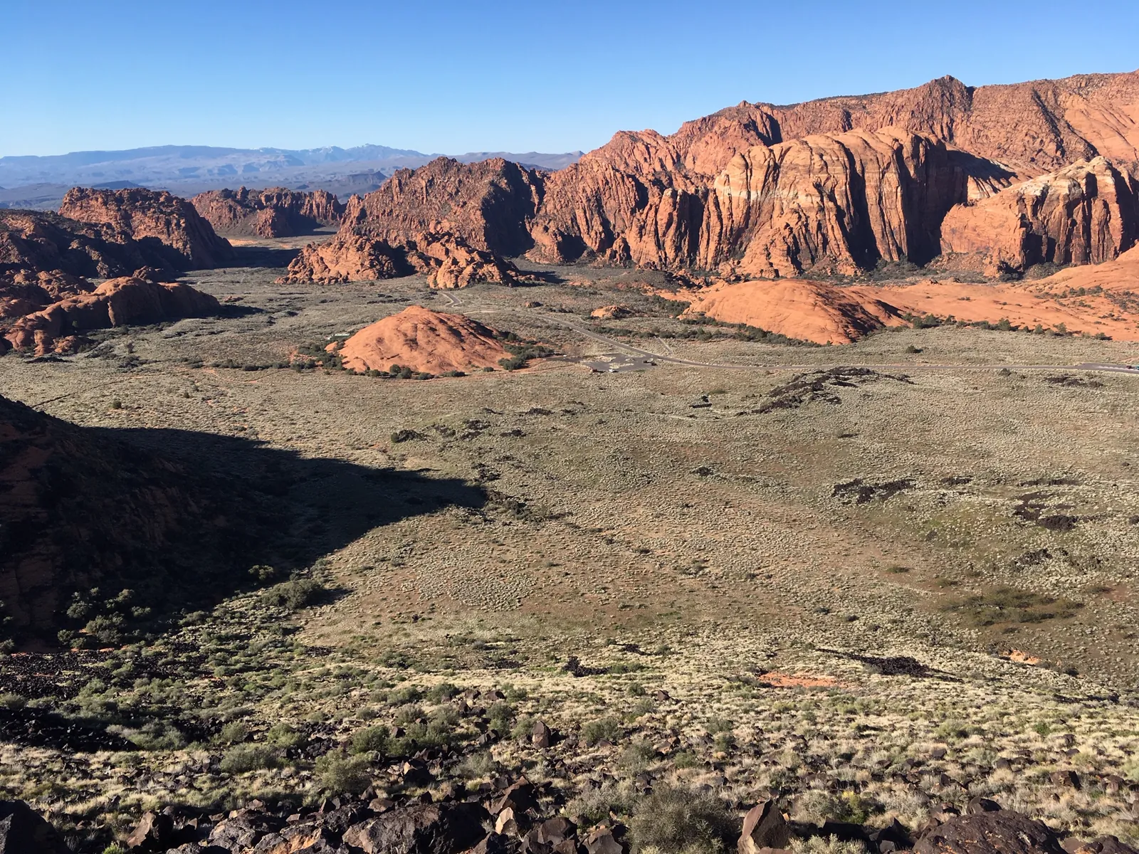 Dark rock and desert shrubs in the foreground with red and white sandstone cliffs behind, Snow Canyon State Park in March.