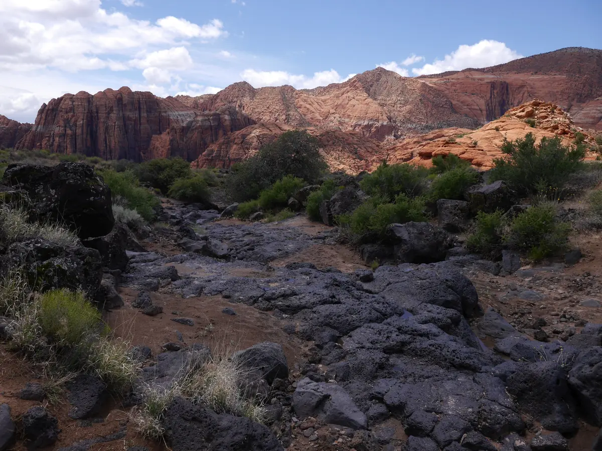 A dark, broken lava flow crossing the canyon floor below red cliffs in Snow Canyon State Park.
