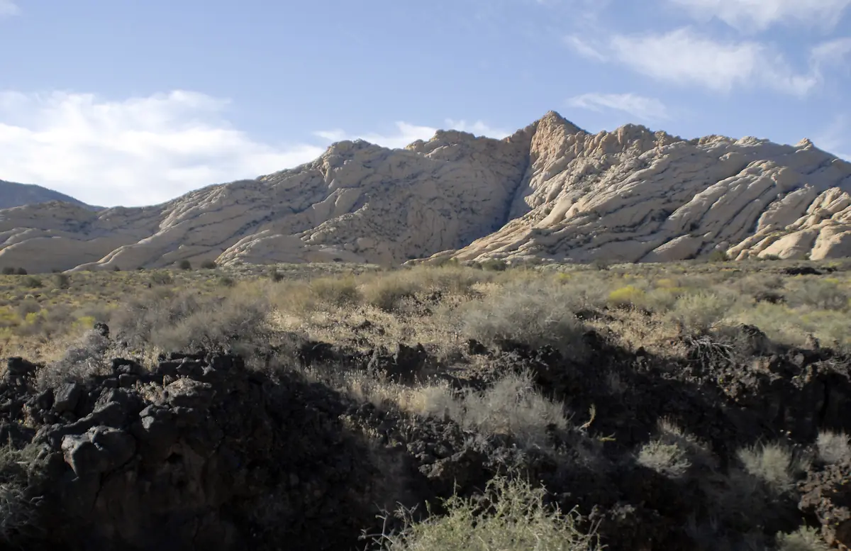 Dark lava rock in the foreground with jagged white and red sandstone peaks behind, Snow Canyon State Park.