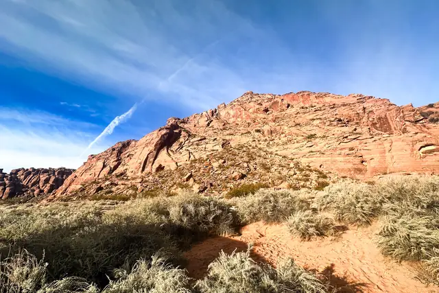 Morning sun on a red sandstone hill above golden grass and a sandy trail in Snow Canyon State Park.