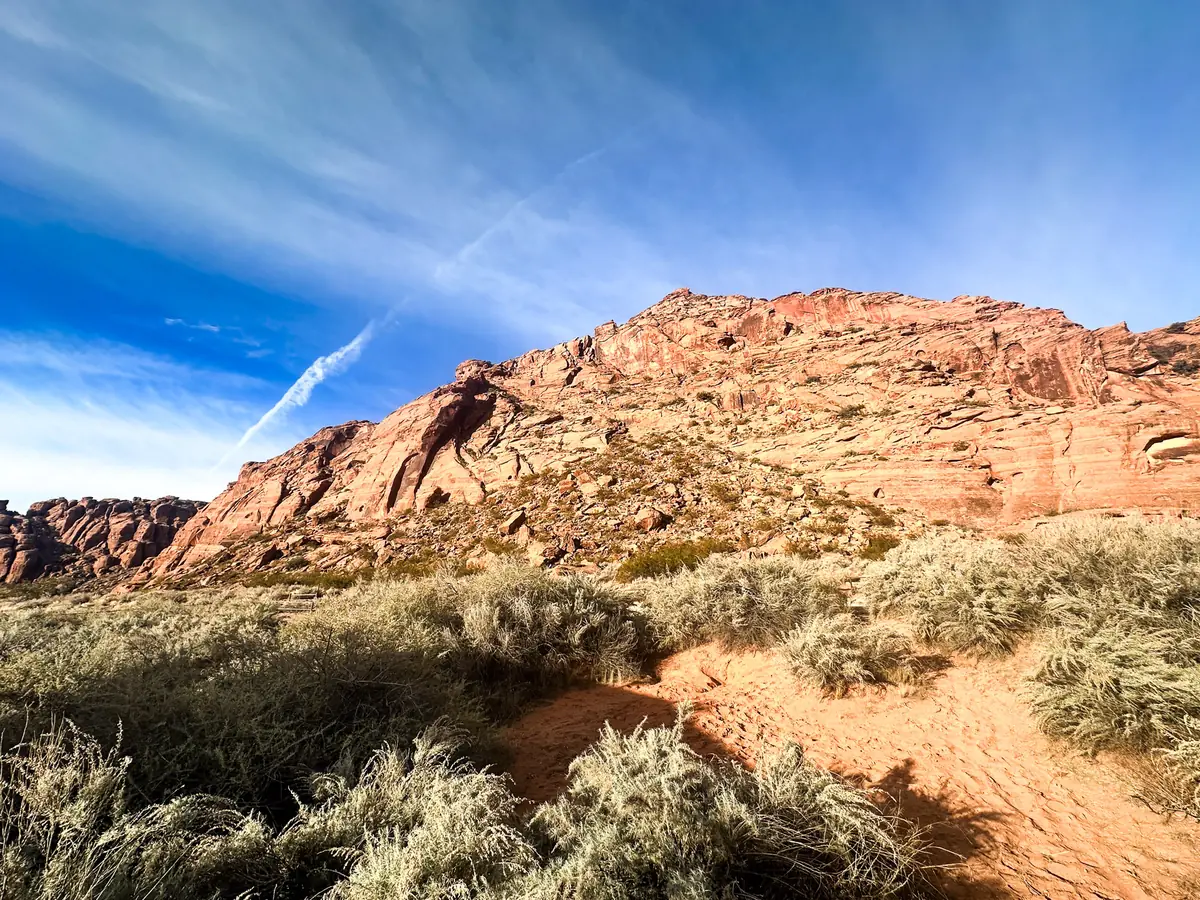 Morning sun on a red sandstone hill above golden grass and a sandy trail in Snow Canyon State Park.