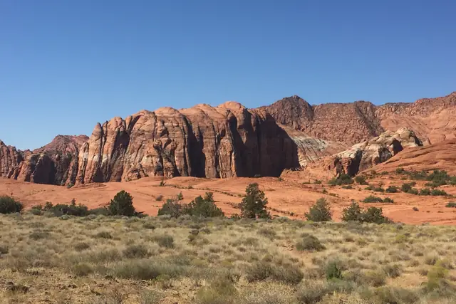 Red and white sandstone cliffs rising above a grassy desert meadow in Snow Canyon State Park.