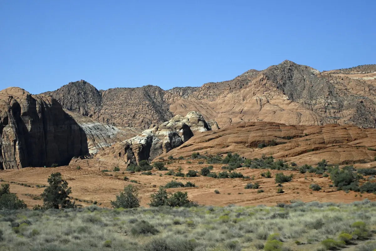 Dark rock outcrops and layered sandstone cliffs above desert grassland in Snow Canyon State Park.