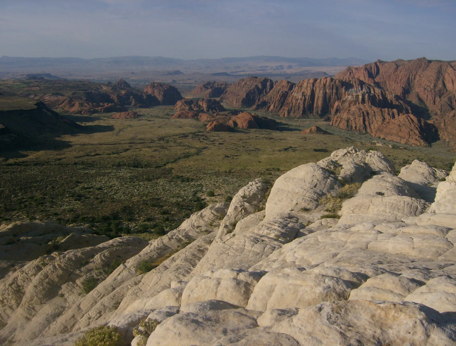 Pale sandstone domes in front of a long line of red cliffs in Snow Canyon State Park.