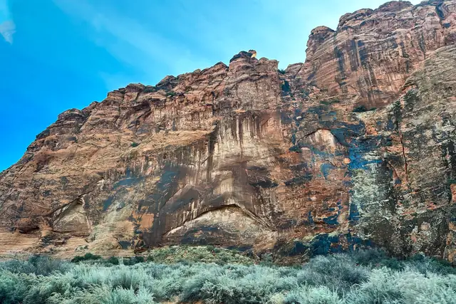 A tall streaked red-and-white sandstone cliff above pale shrubs in Snow Canyon State Park.