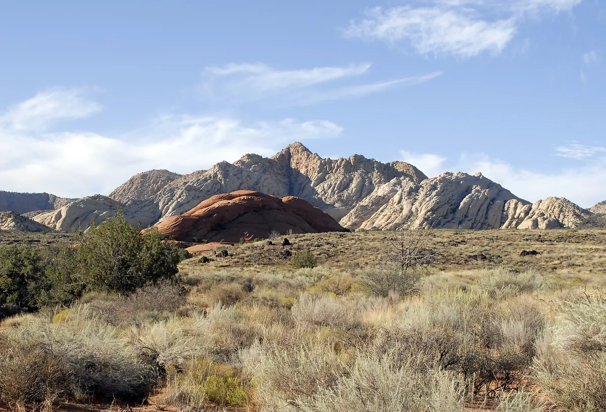 Grassy desert below jagged white and red sandstone peaks in evening light, Snow Canyon State Park.